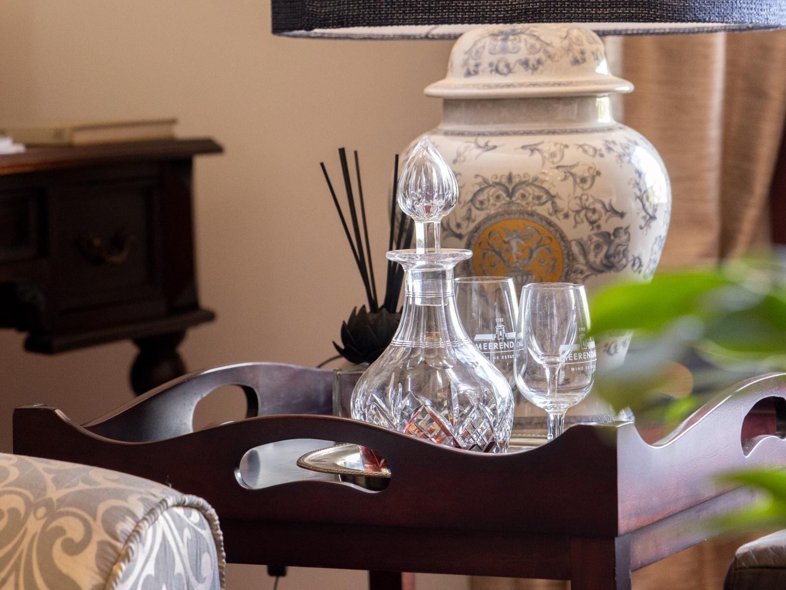 A tray with a crystal decanter, two wine glasses, and a decorative vase on a wooden table.