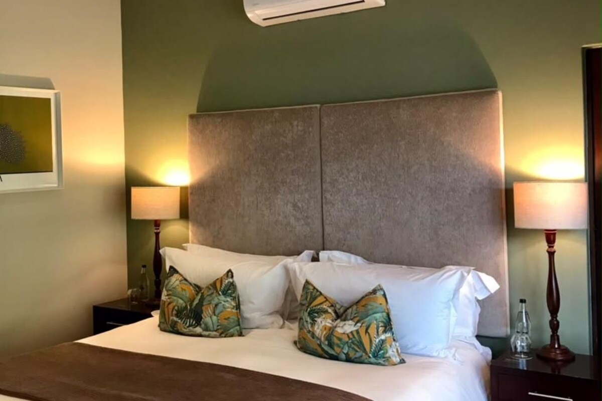Een hotelkamer met een groot bed, twee bedlampen, een wandairconditioner en een ingelijst schilderij aan de muur.