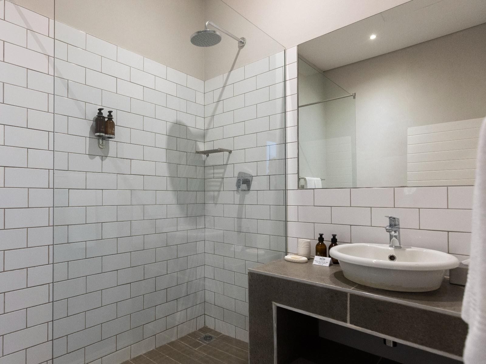 A modern bathroom with white subway tiles, a glass shower enclosure, a vanity with a sink, and a mirror.