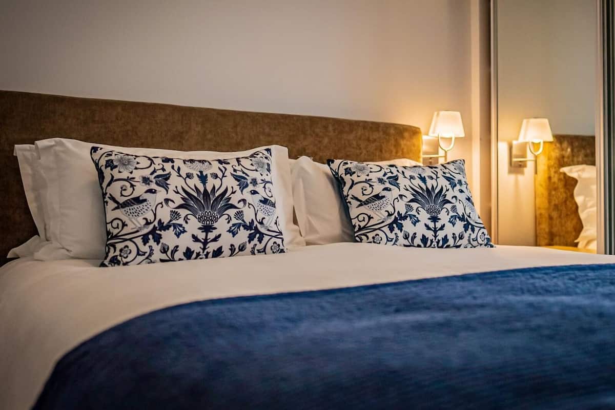A hotel room with a bed, two decorative pillows, a headboard, and two wall-mounted lamps.