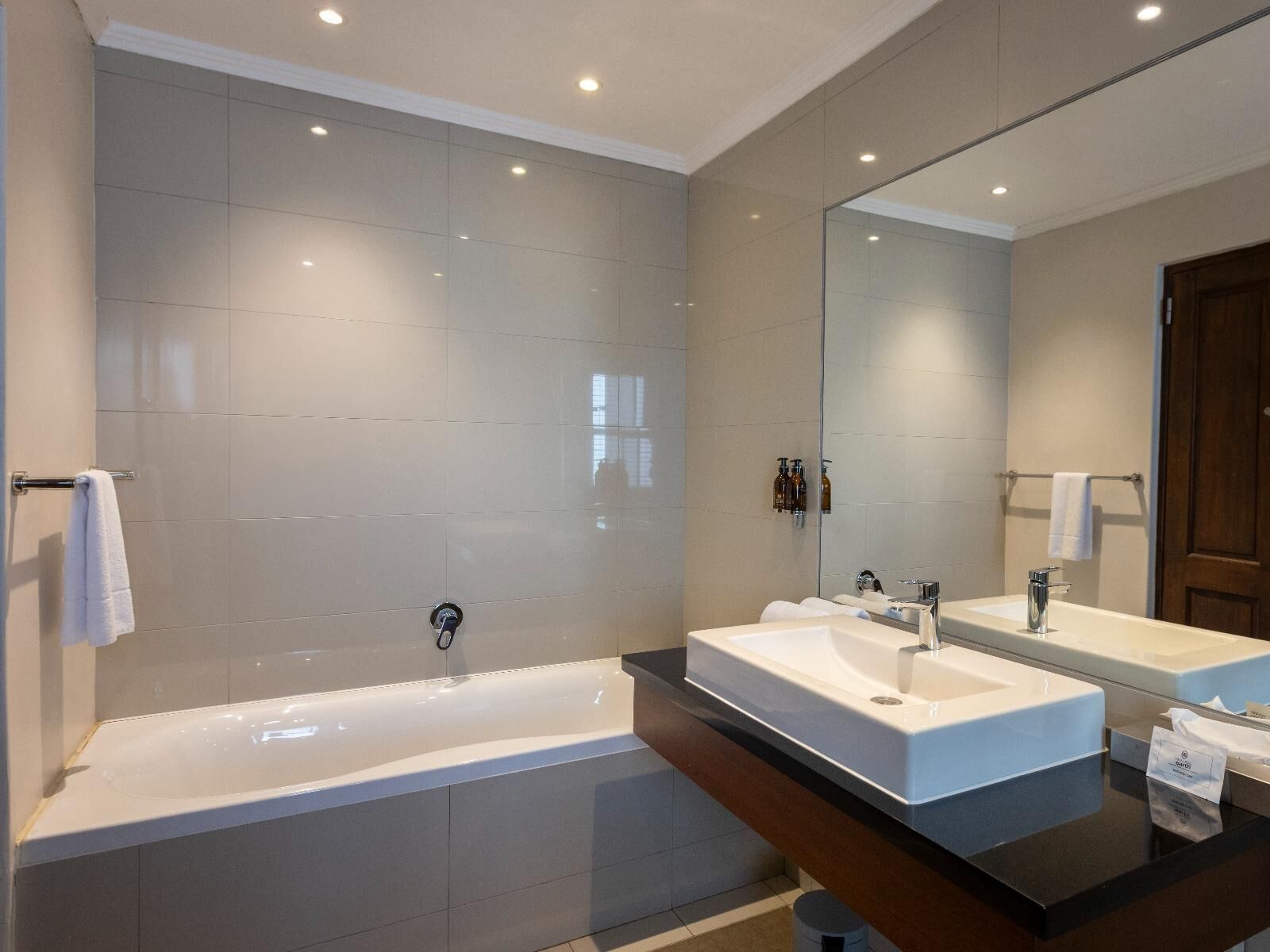 A modern bathroom with a large bathtub, two sinks, and a mirror.