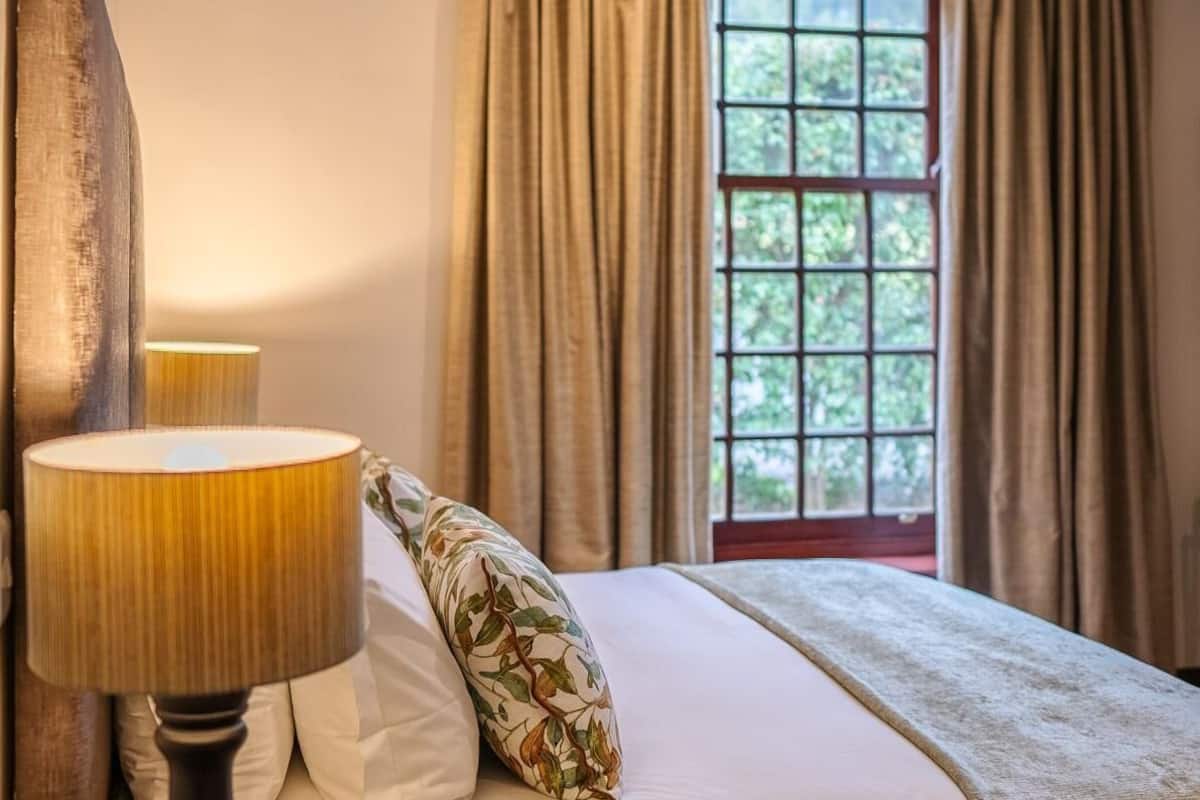 A bed with a floral pillow, a lamp, and a window with curtains.