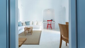 A minimalist living room with a white sofa, a wooden coffee table, a red chair, and a small desk with a chair. - Helestia Pocket Hotel, Caldera Santorini (Santorini)