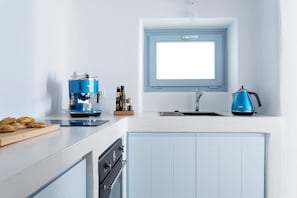 A kitchen with a blue coffee maker, a kettle, and a cutting board with pastries. - Helestia Pocket Hotel, Caldera Santorini (Santorini)