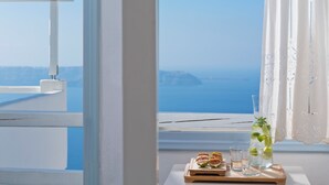 A view through a window with a table holding a pitcher, glasses, and a wooden tray with food items. - Helestia Pocket Hotel, Caldera Santorini (Santorini)