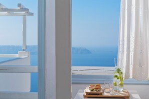 A view through a window with a table holding a pitcher, glasses, and a wooden tray with food items. - Helestia Pocket Hotel, Caldera Santorini (Santorini)