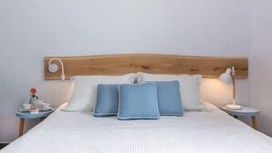 A neatly made bed with a wooden headboard, two bedside tables with lamps, and a small table with a flower and a cup. - Helestia Pocket Hotel, Caldera Santorini (Santorini)