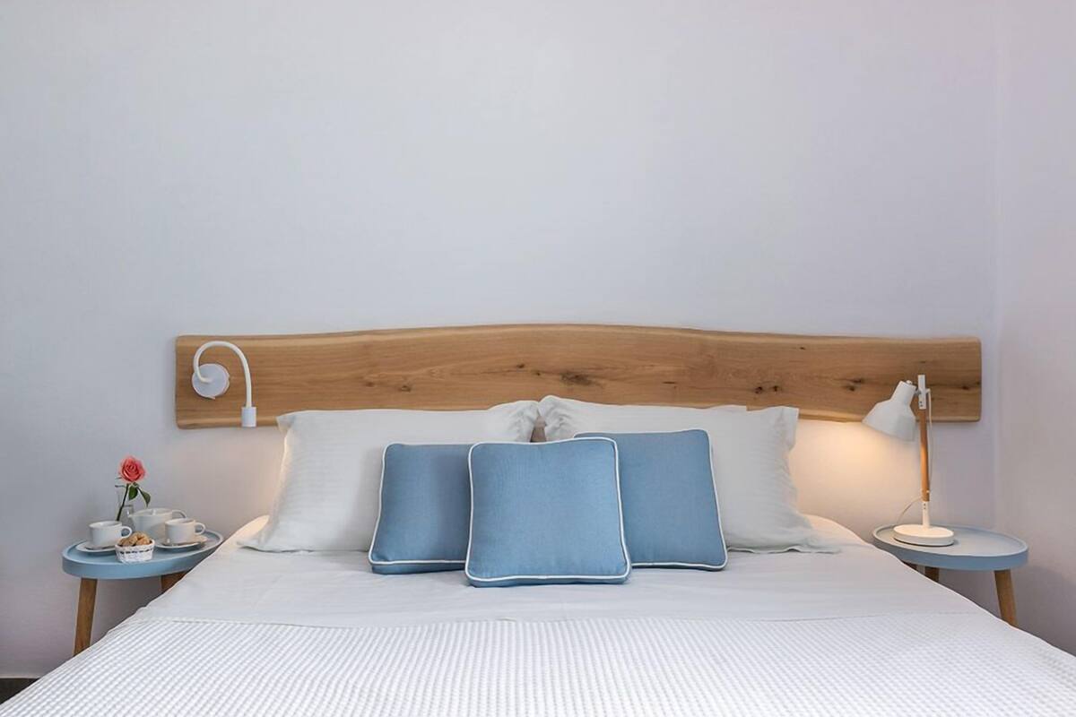 A neatly made bed with a wooden headboard, two bedside tables with lamps, and a small table with a flower and a cup.