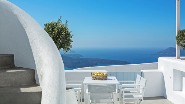 A white outdoor seating area with a table and chairs, a basket of bread, and a view of the sea. - Helestia Pocket Hotel, Caldera Santorini (Santorini)