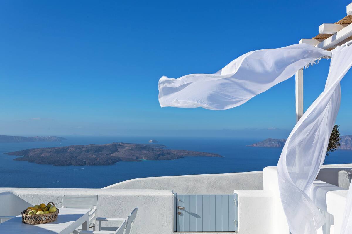 A white balcony with a wicker basket of fruit, overlooking a scenic view of the sea and islands.