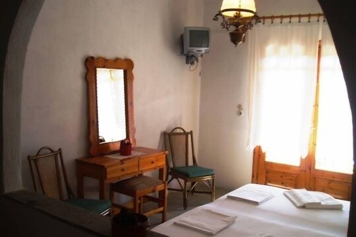 A room with a bed, a wooden dresser, a mirror, a television, and a window with curtains.
