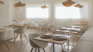 A modern dining area with white furniture, wooden tables, and woven placemats. - Hotel Farol (Ilhavo)