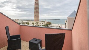 A balcony with wicker chairs and a view of a lighthouse and beach. - Hotel Farol (Ilhavo)