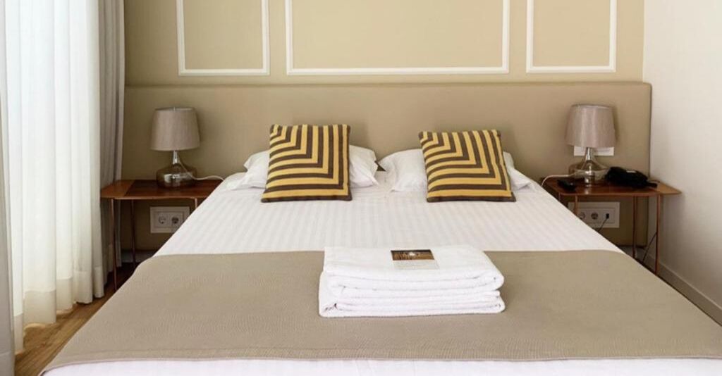 A neatly made bed with striped pillows, a folded towel, and a bedside lamp on each side.