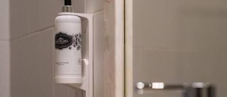 Un baño con dispensador de jabón en la pared, un espejo y un lavamanos con grifo.