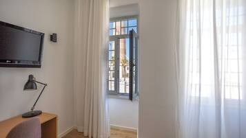 A room with a desk, a chair, a TV, and a window with curtains.