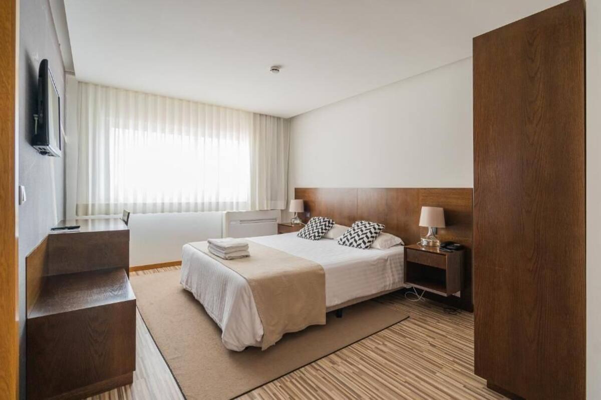 Une chambre d’hôtel avec un lit, des tables de chevet, une télévision et une fenêtre avec des rideaux.