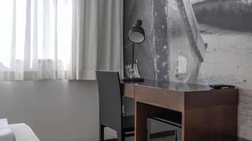 Habitación de hotel con cama, escritorio, silla, televisor y un amplio ventanal con cortinas.