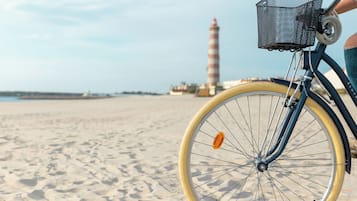 Een fiets met een mandje op een zanderig strand, met een vuurtoren op de achtergrond.