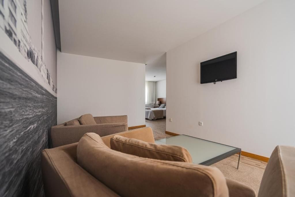 A modern living room with a sofa, a glass coffee table, and a flat-screen TV mounted on the wall.