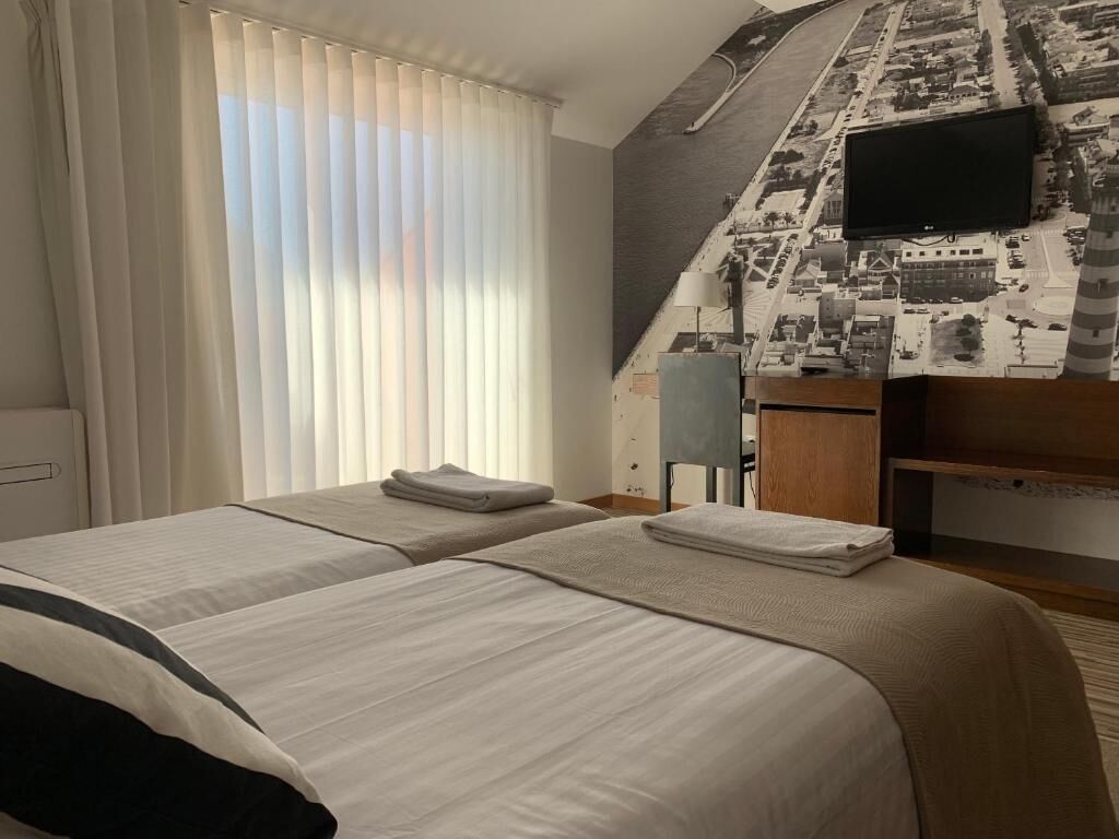 Habitación de hotel con dos camas, un ventanal grande con cortinas, un televisor de pantalla plana montado en la pared y una escalera con un mural de paisaje urbano.