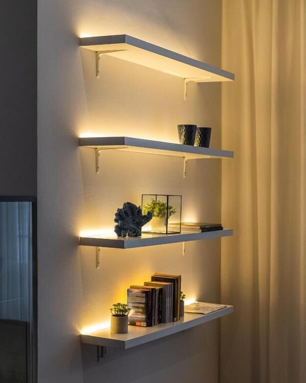A wall-mounted shelf unit with three shelves, each holding decorative items and books. - Hotel Farol (Ilhavo)