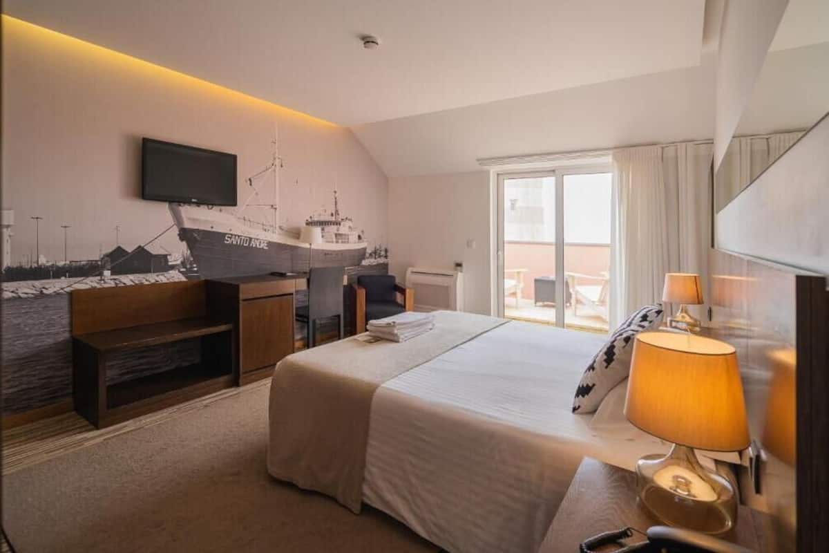 Une chambre d’hôtel équipée d’un lit, d’un bureau, d’une chaise, d’un téléviseur fixé au mur et d’une grande fenêtre.