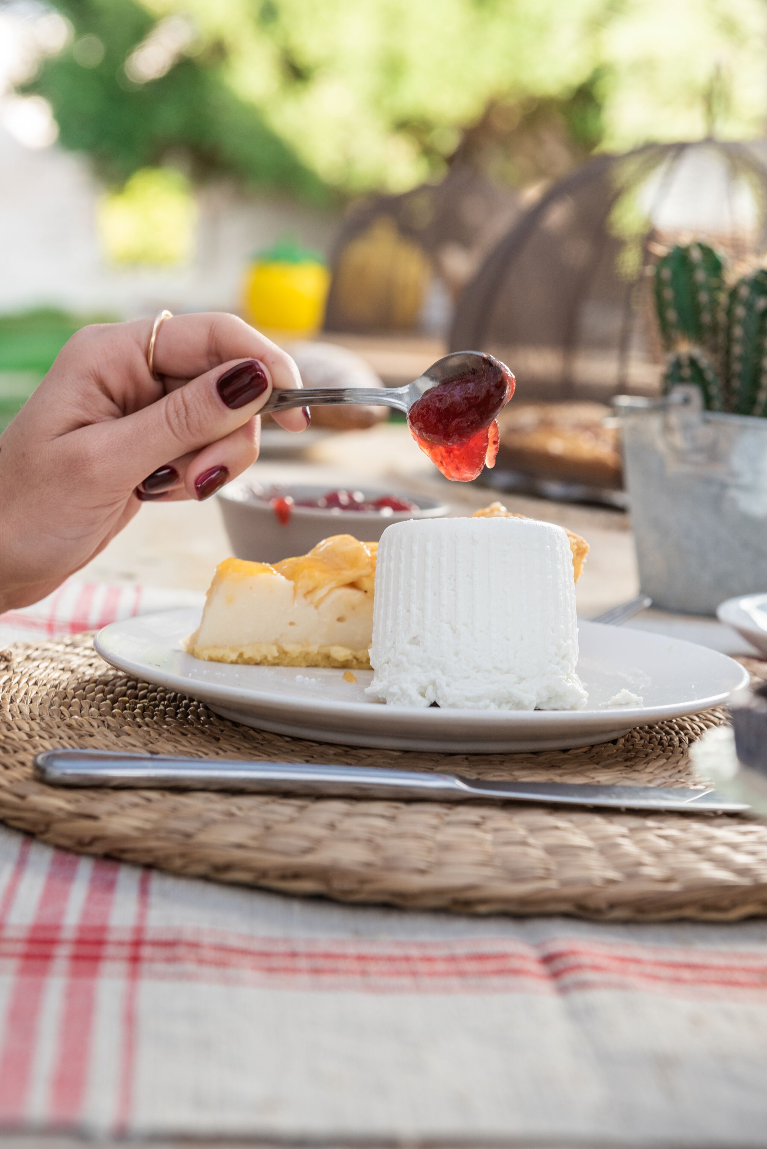 Un plato de postre con una porción de tarta de queso y una bola de helado sobre un posavasos tejido.
