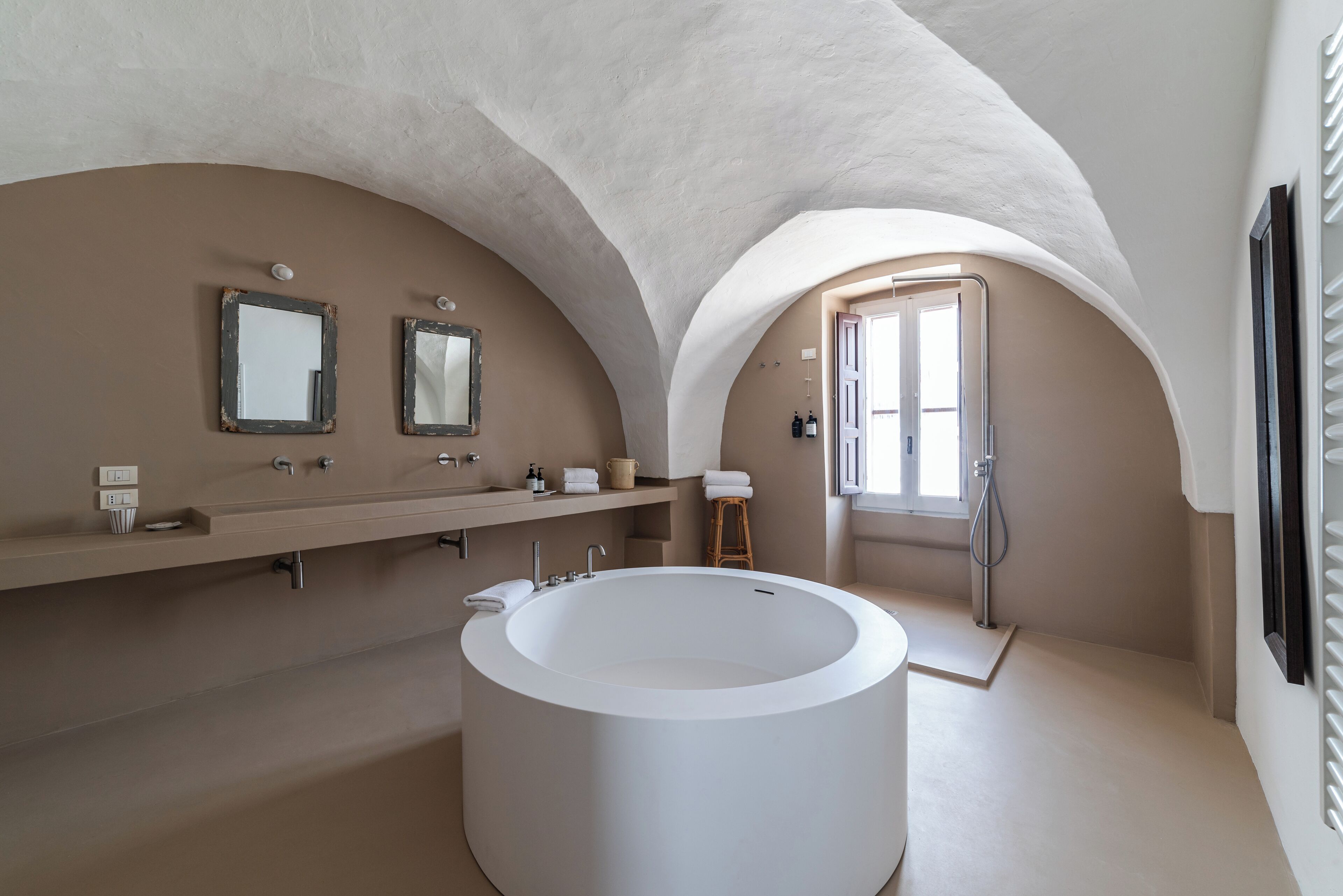 A modern bathroom with a large freestanding bathtub, two wall-mounted mirrors, and a shower area.