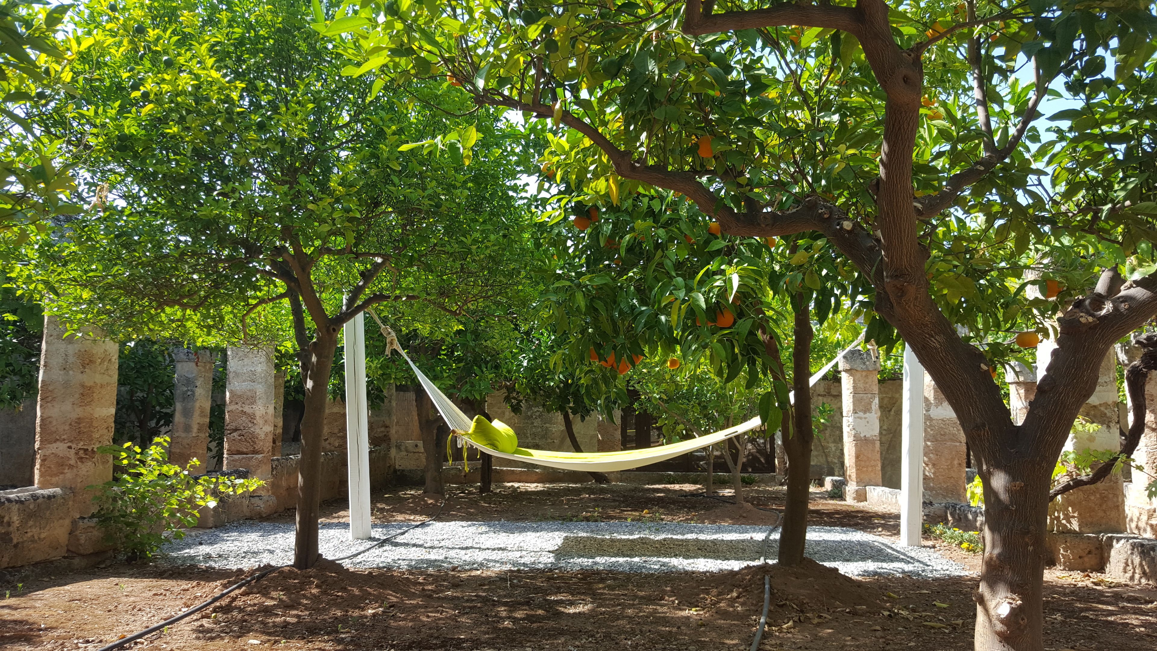 A hammock between trees in a garden with a gravel path and stone walls.