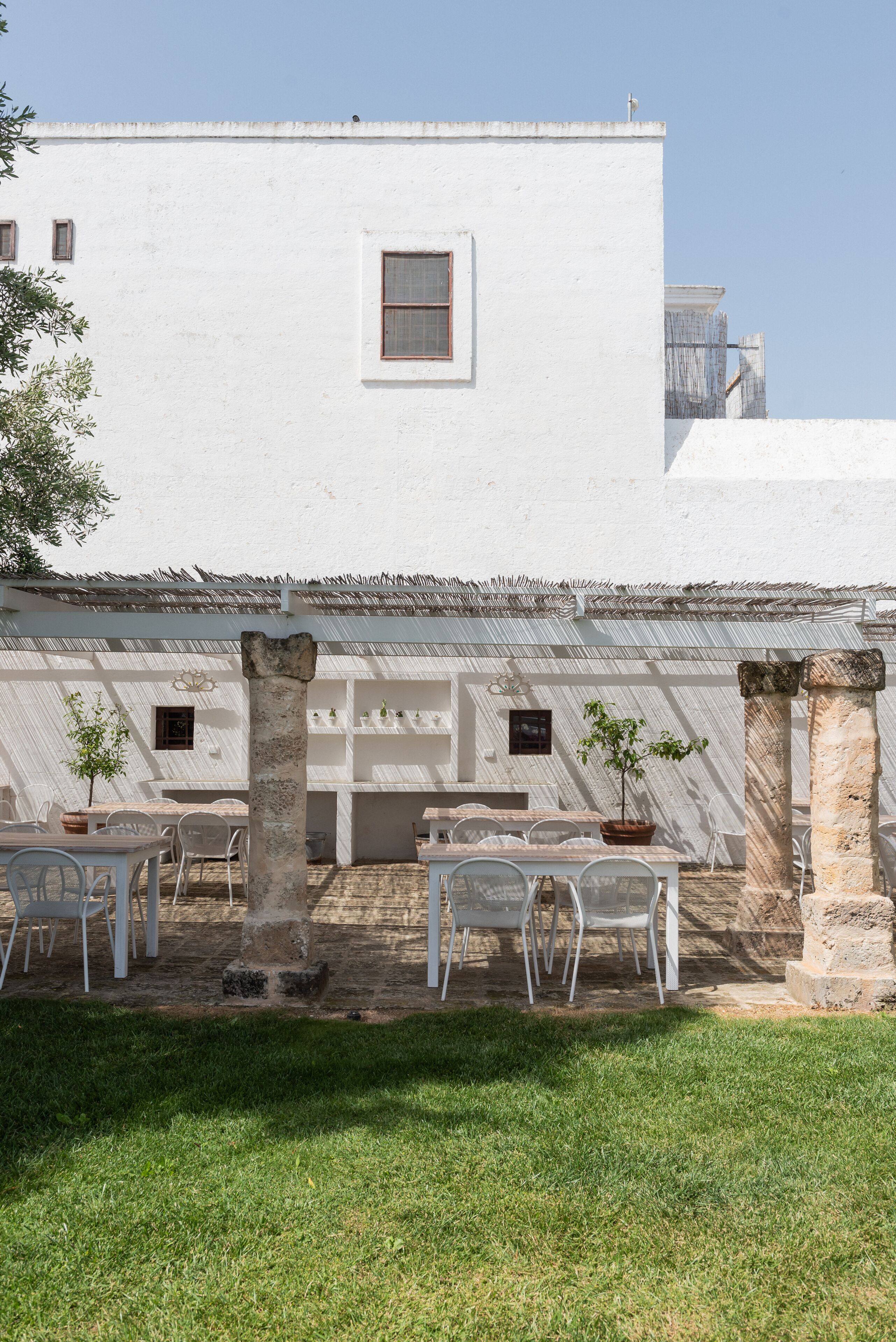 Un patio con paredes blancas, columnas de piedra y mobiliario para exterior.