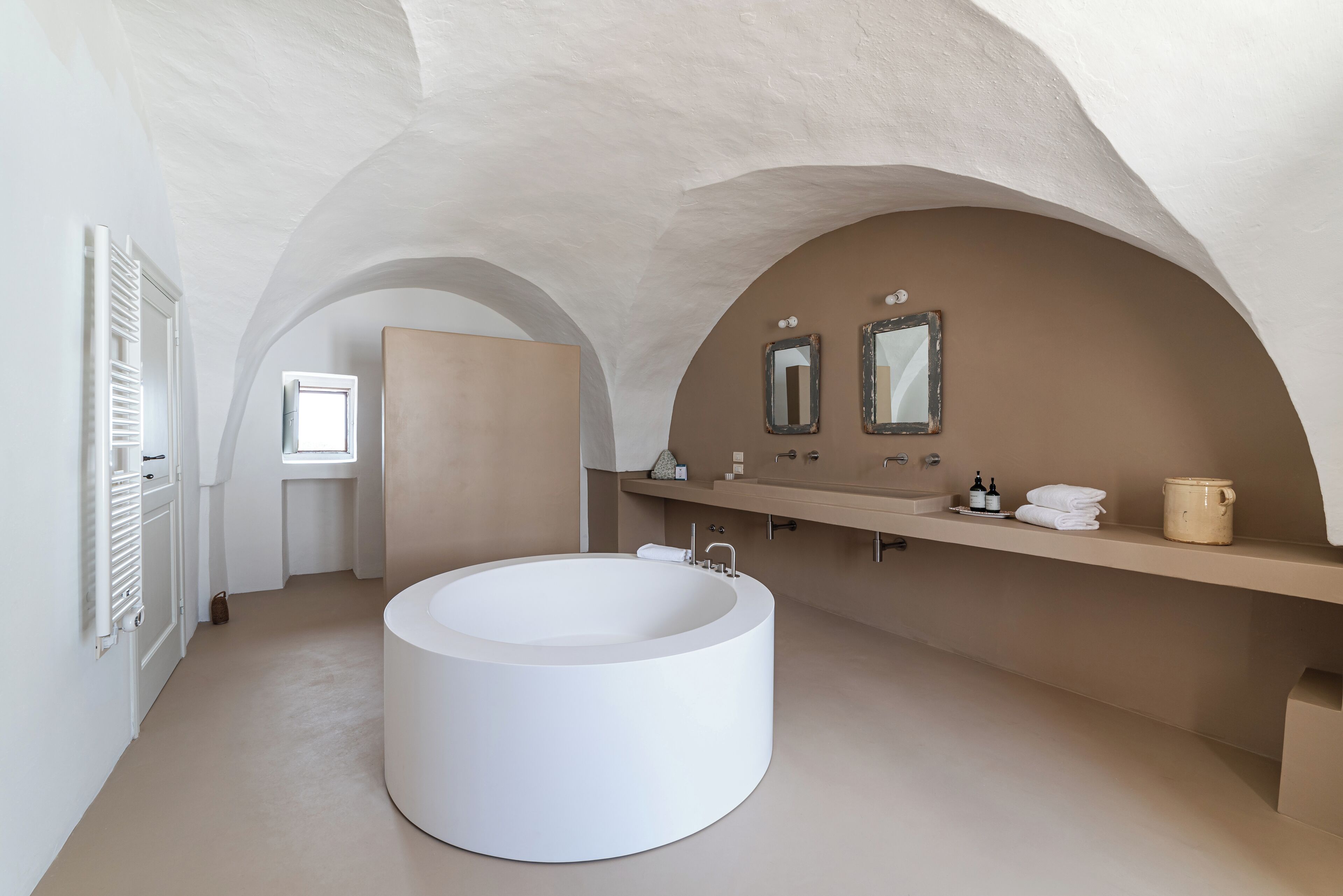 A modern bathroom with a large round bathtub, a vanity with a mirror, and a window.