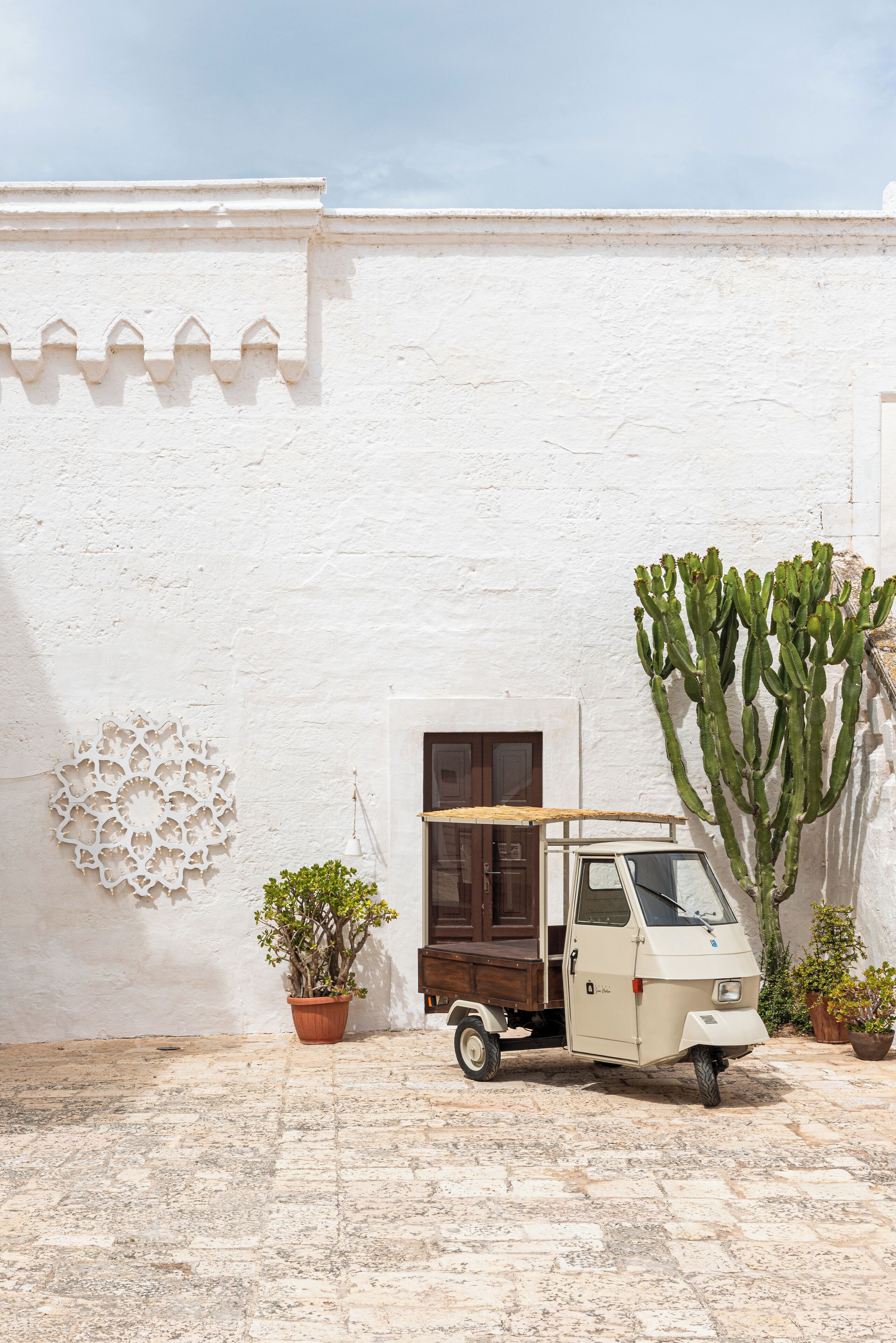 A small, white-walled building with a parked vehicle and a large cactus.