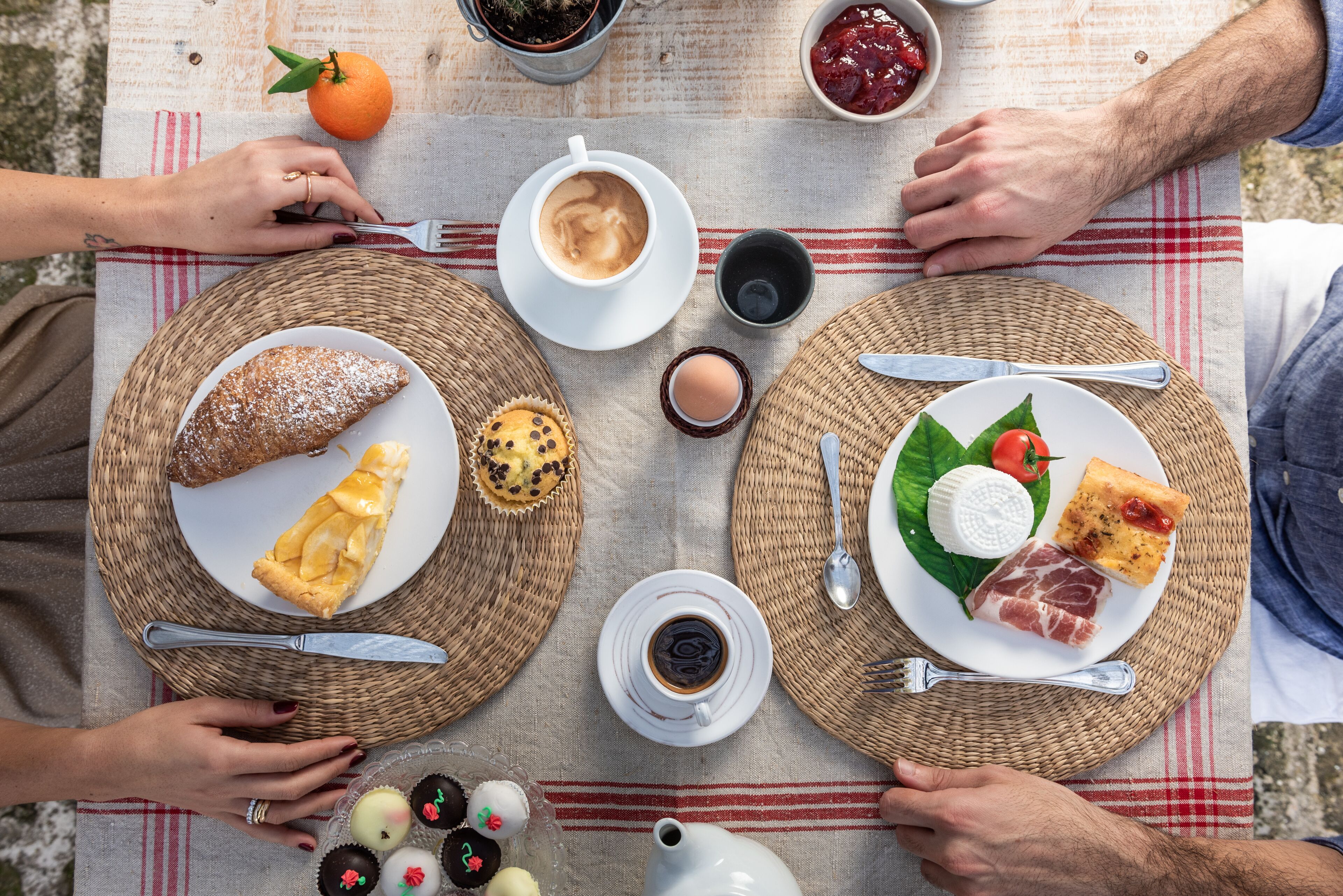 Een picknickopstelling met borden vol eten, koffiebekers en een theepot op een tafelkleed.