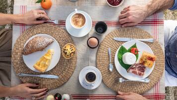 Een picknickopstelling met borden vol eten, koffiebekers en een theepot op een tafelkleed.