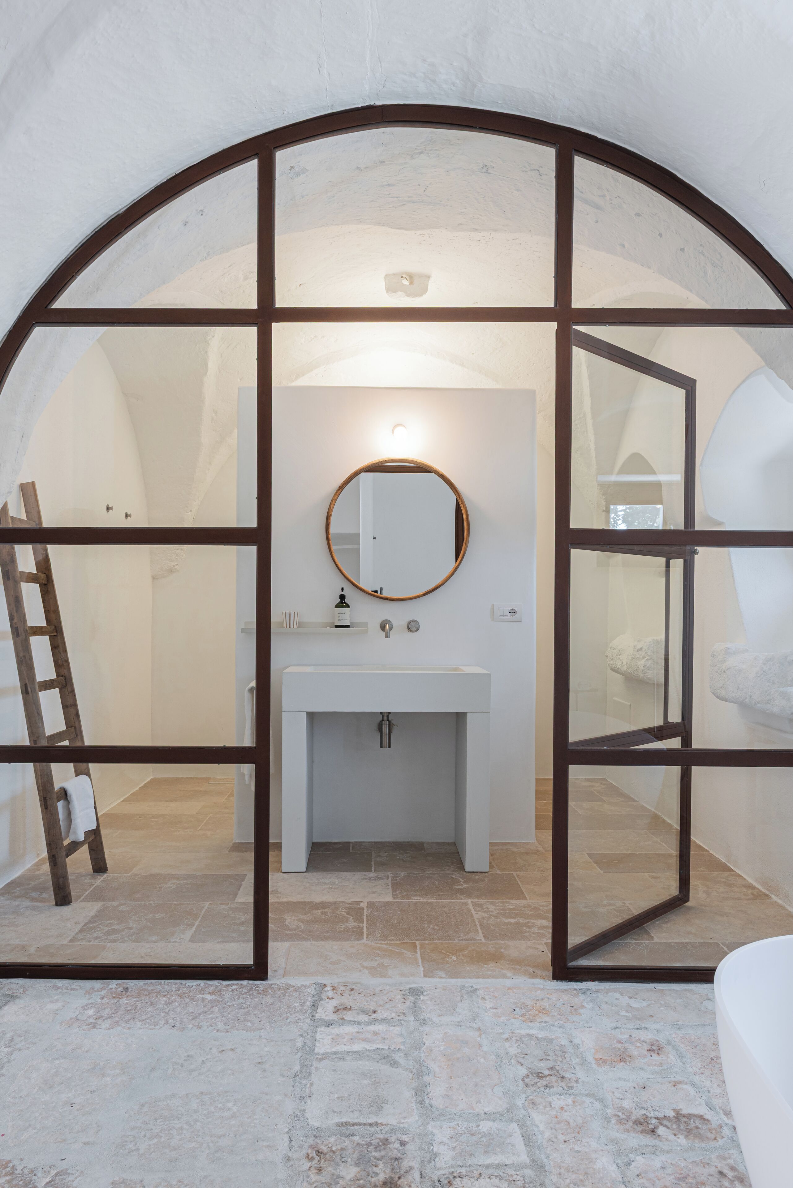 A bathroom with a white sink, a round mirror, and a shower area.
