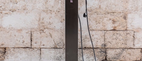 A black electric vehicle charging station with the Porsche logo, mounted on a concrete base against a textured wall.