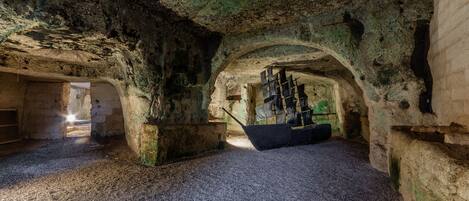 An underground room with a ship model and a person standing near an archway.