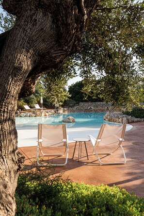 Un área de piscina con sillones de descanso, un muro de piedra y follaje.