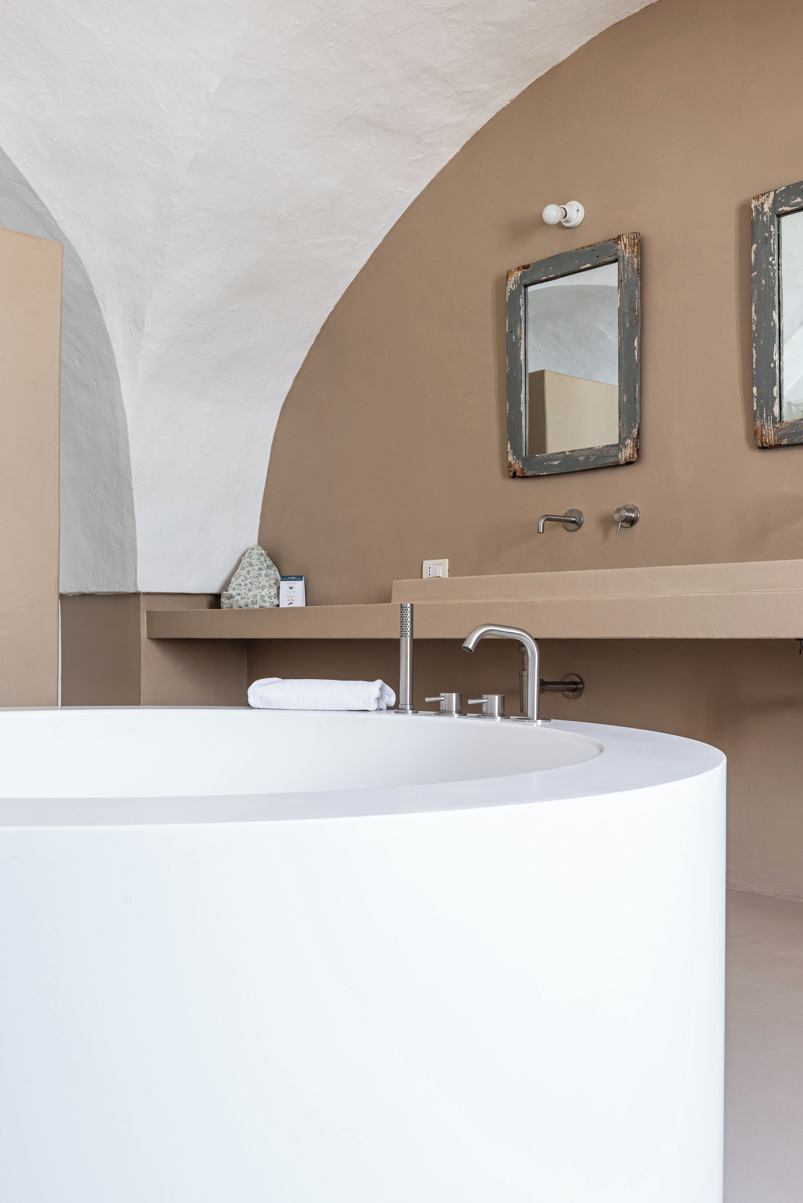 Une salle de bain moderne avec une grande baignoire blanche, un meuble-lavabo beige et deux miroirs aux cadres vieillis.