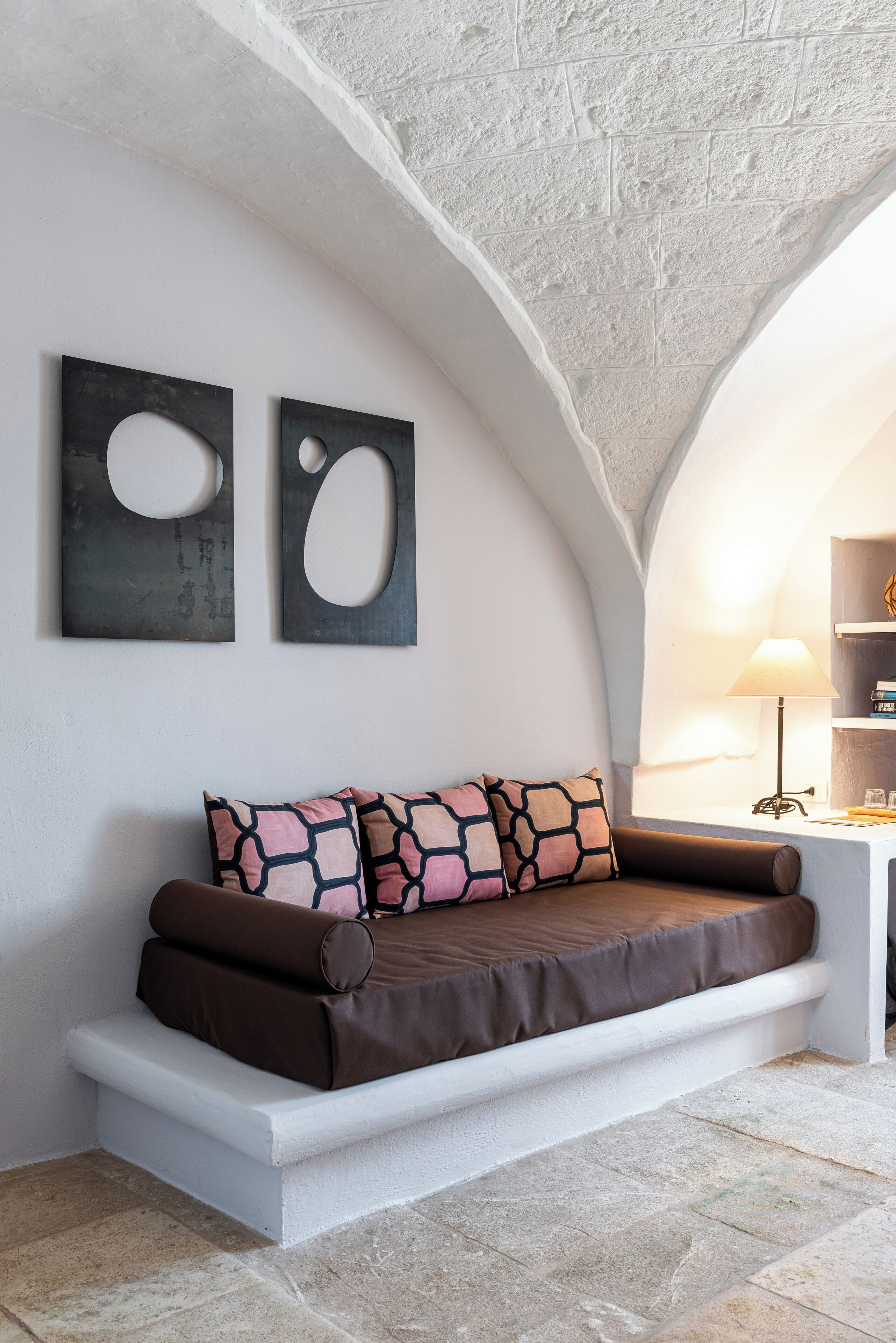 A cozy seating area with a cushioned bench, a lamp, and two abstract wall art pieces.
