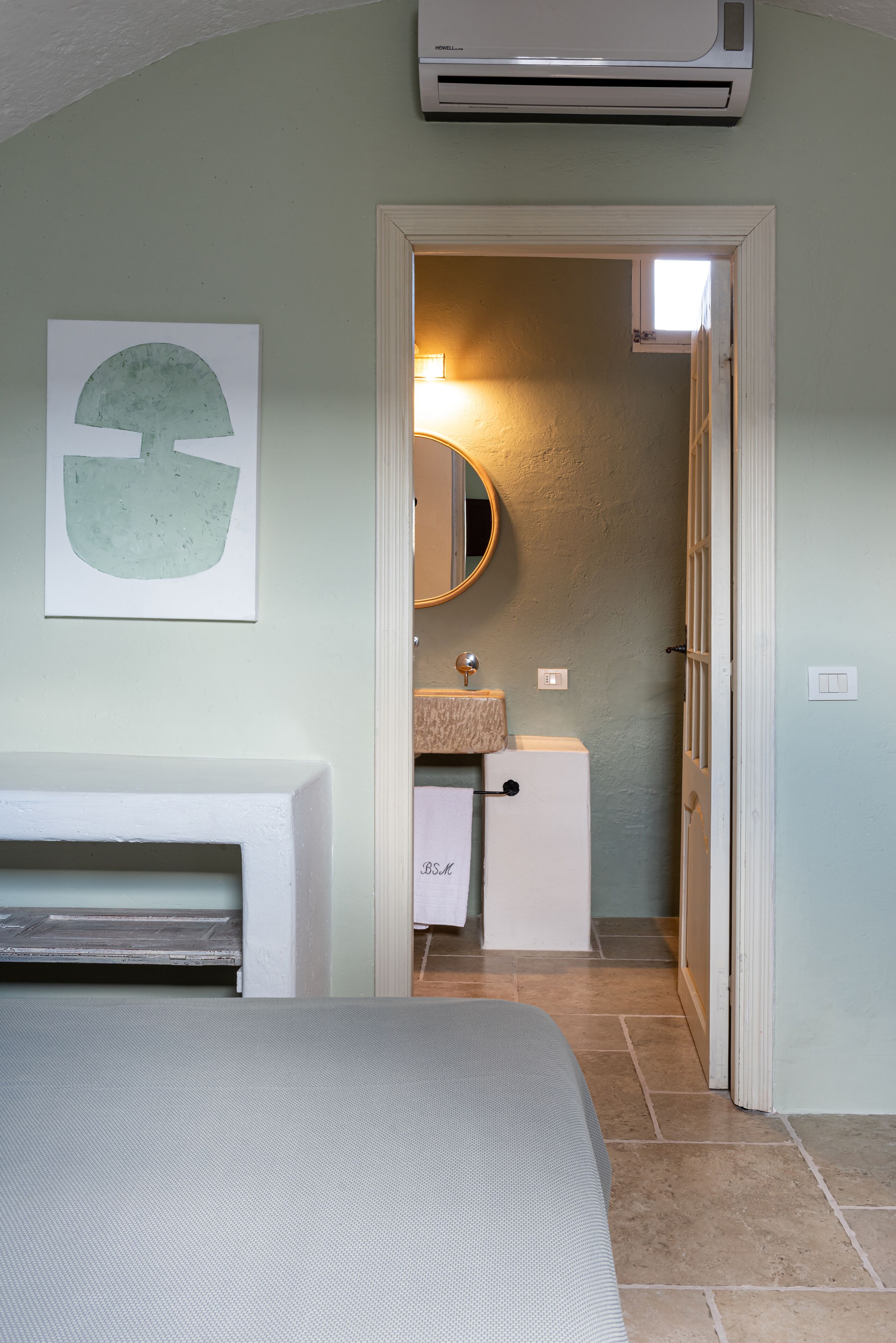 Un dormitorio con cama, un baño con lavabo y espejo, y un equipo de aire acondicionado.