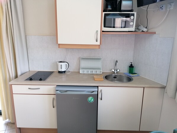 Een kleine keuken met een magnetron, waterkoker, spoelbak en een compacte koelkast.