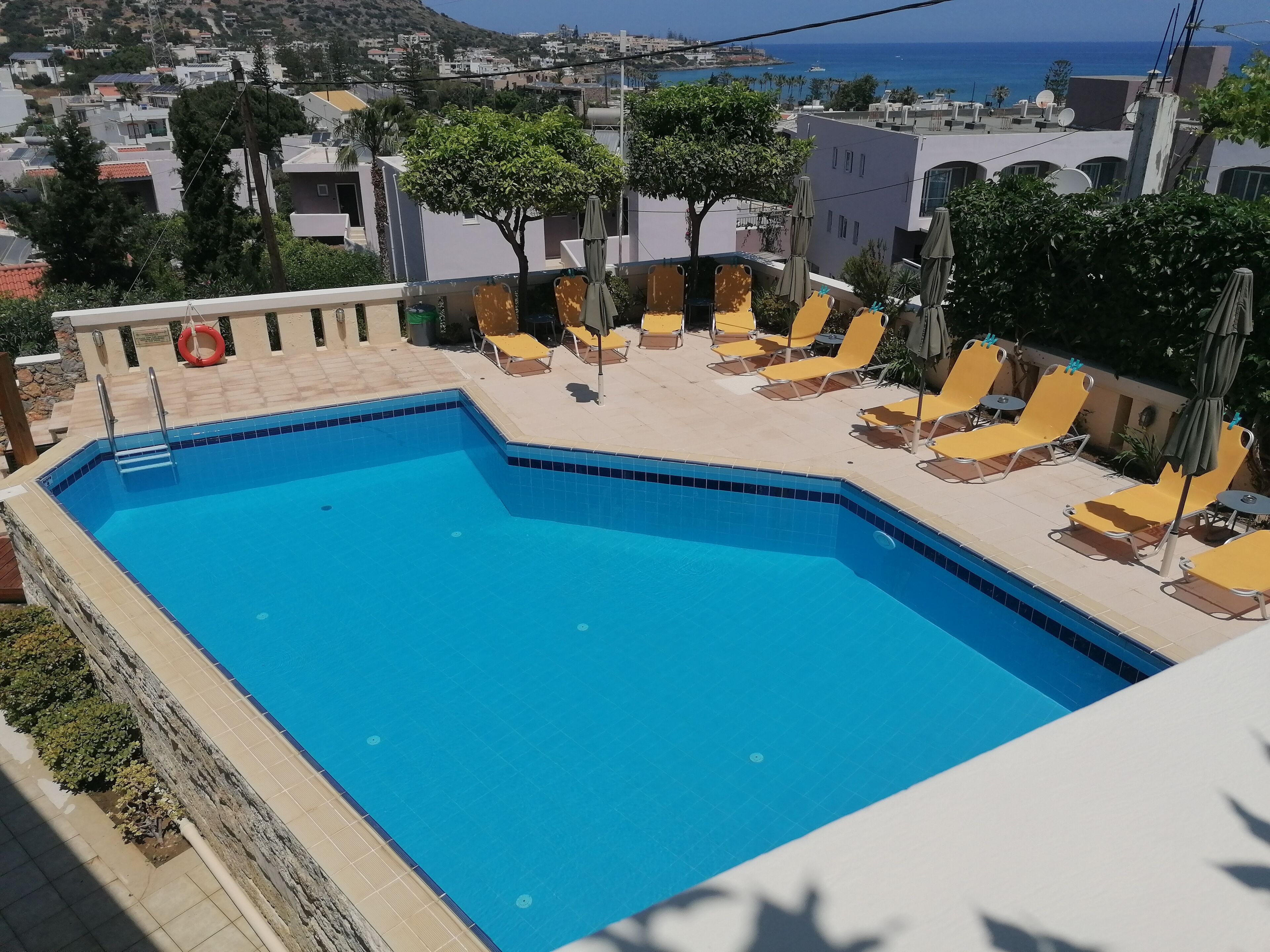 A rectangular swimming pool with a tiled edge, surrounded by yellow lounge chairs and umbrellas.