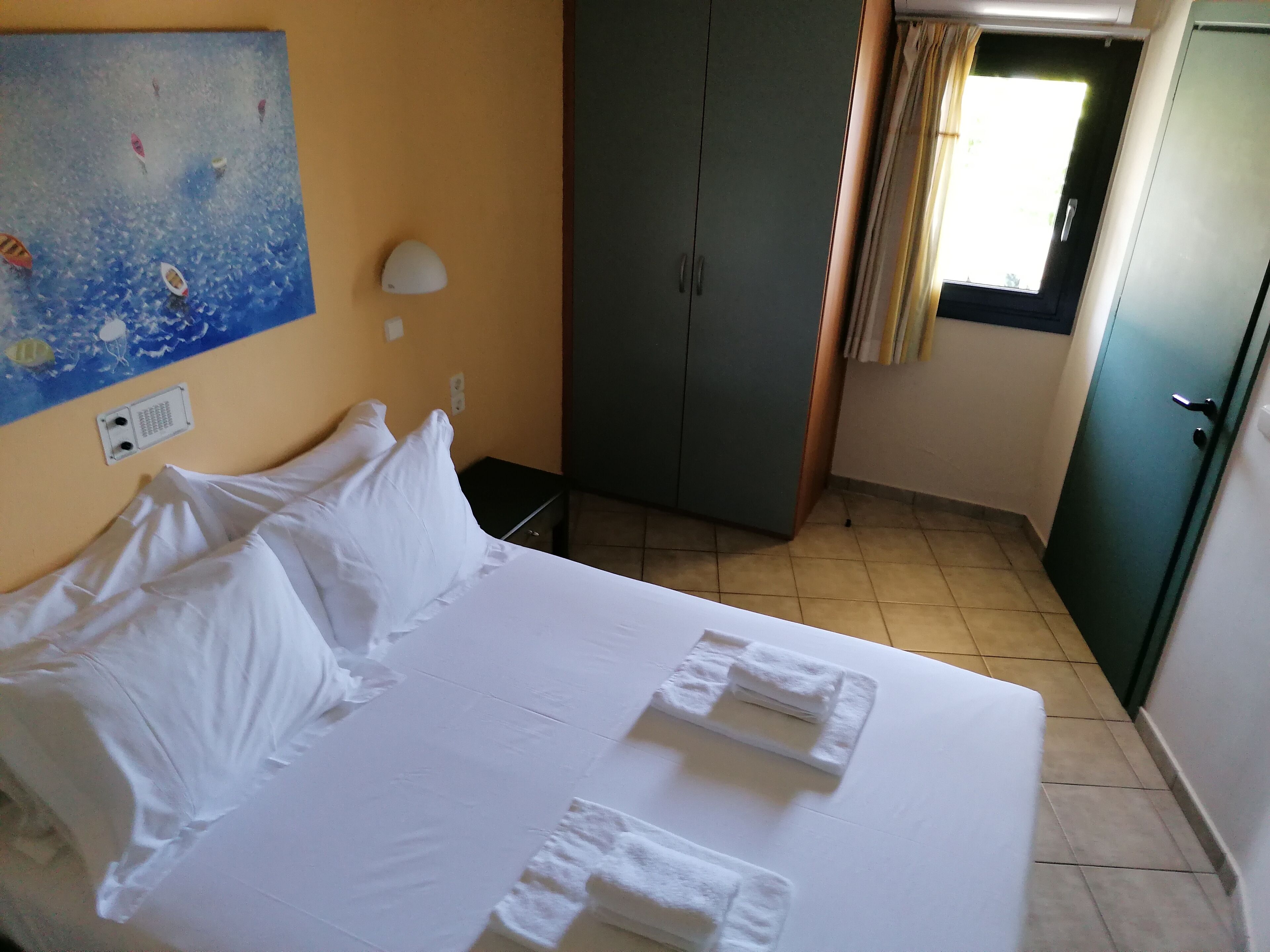 Una habitación de hotel con cama, almohadas, mesita de noche, armario y un cuadro en la pared.
