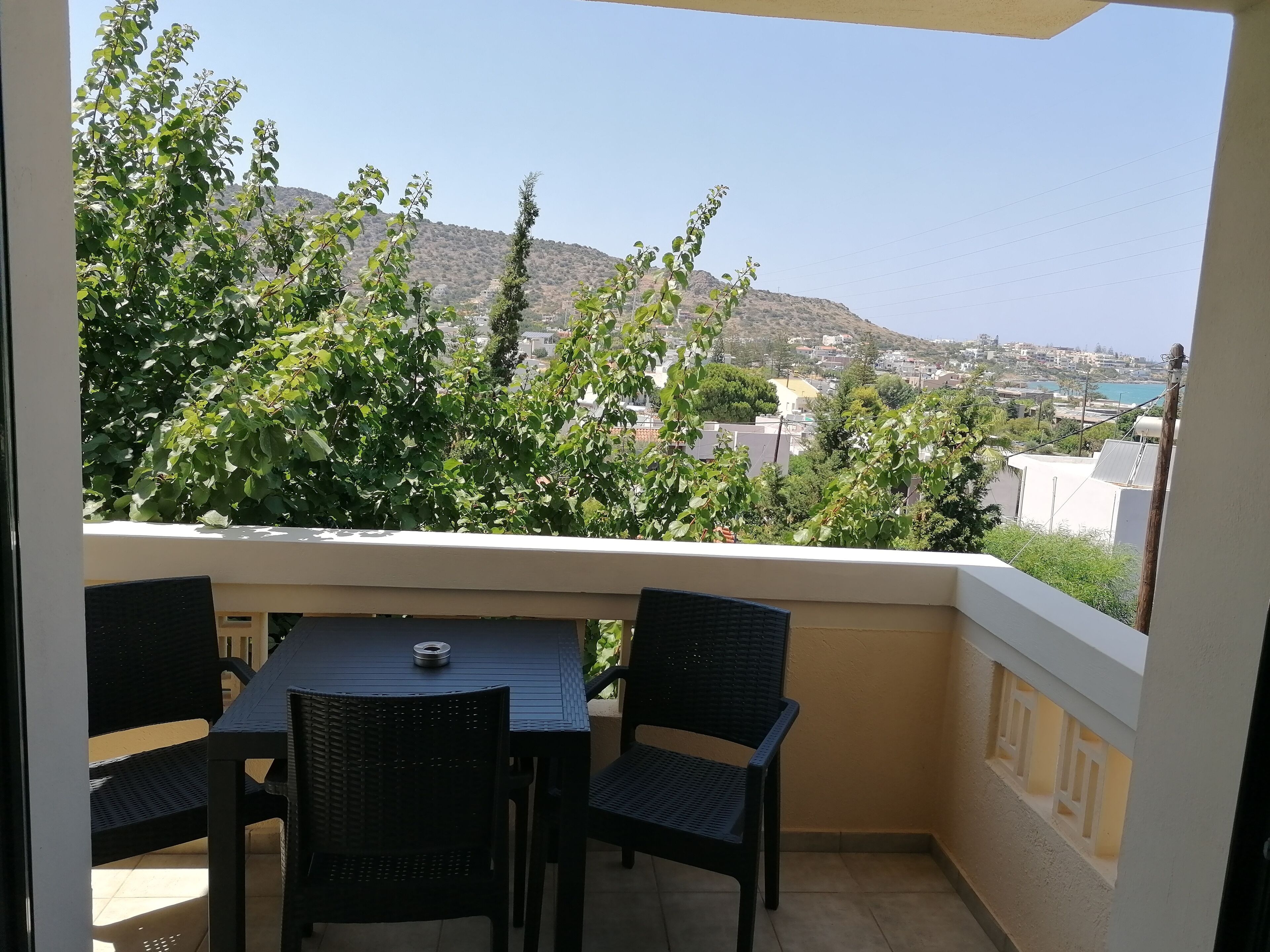 A balcony with a table and chairs, overlooking a hillside with buildings and greenery.