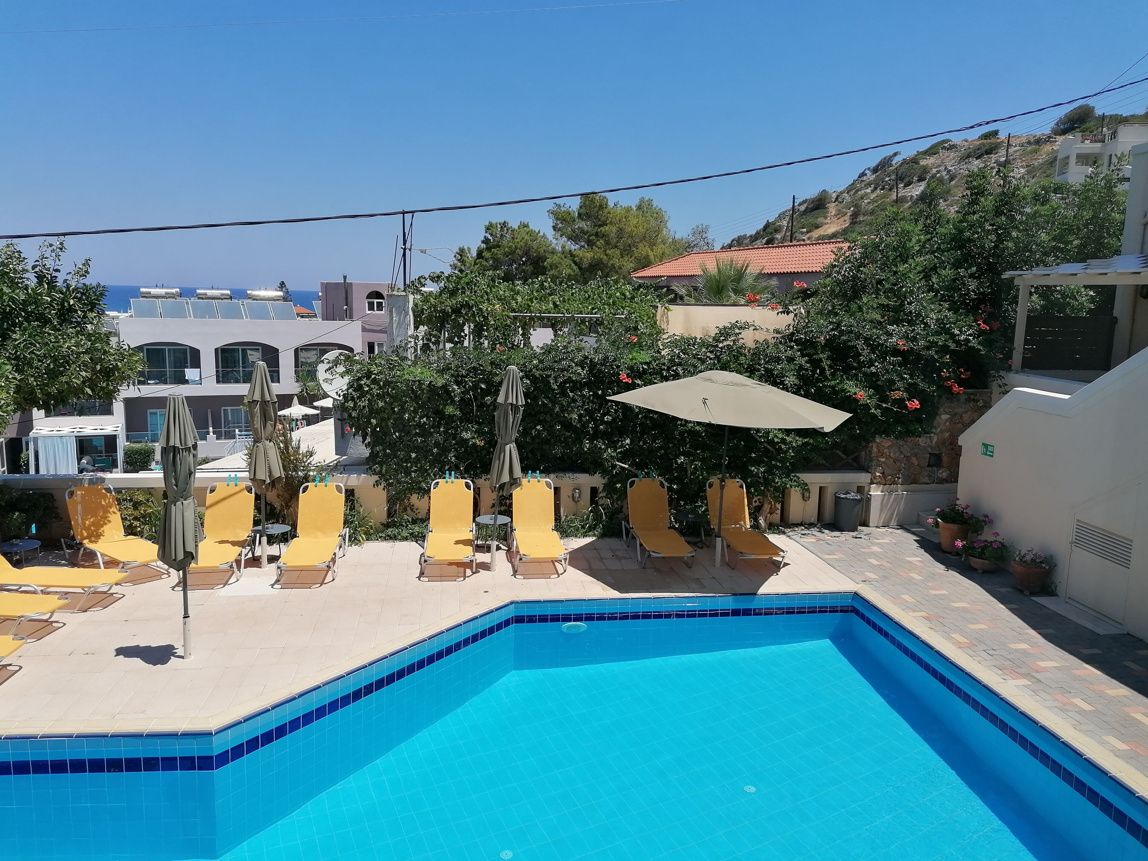 Una piscina con sillas de sol amarillas y una sombrilla, rodeada de edificios y árboles.