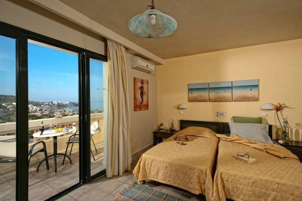 A hotel room with two beds, a balcony with a table and chairs, and a city view.