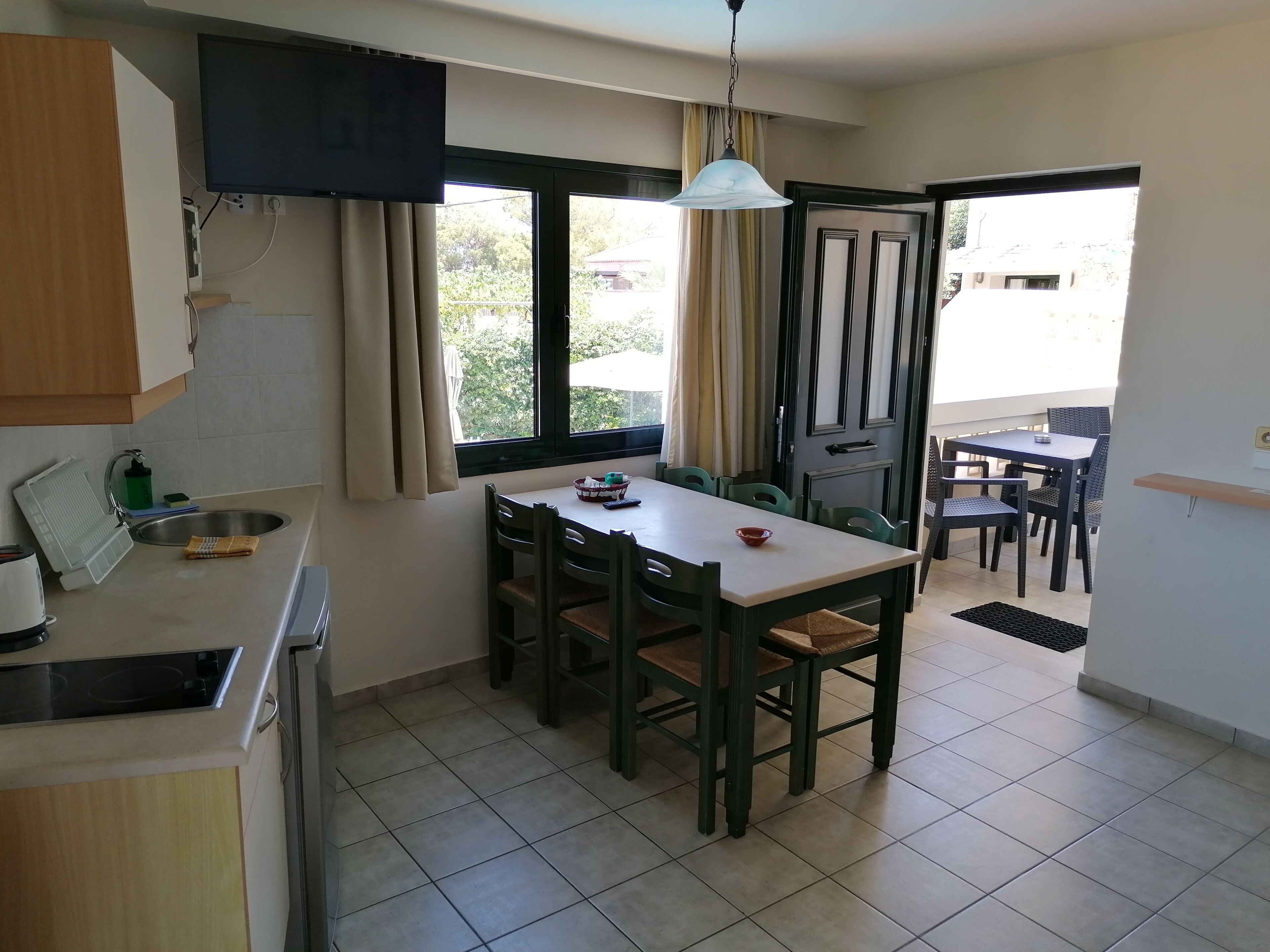 A compact kitchen with a dining area, a TV mounted above the counter, and a view of the outside through the window.