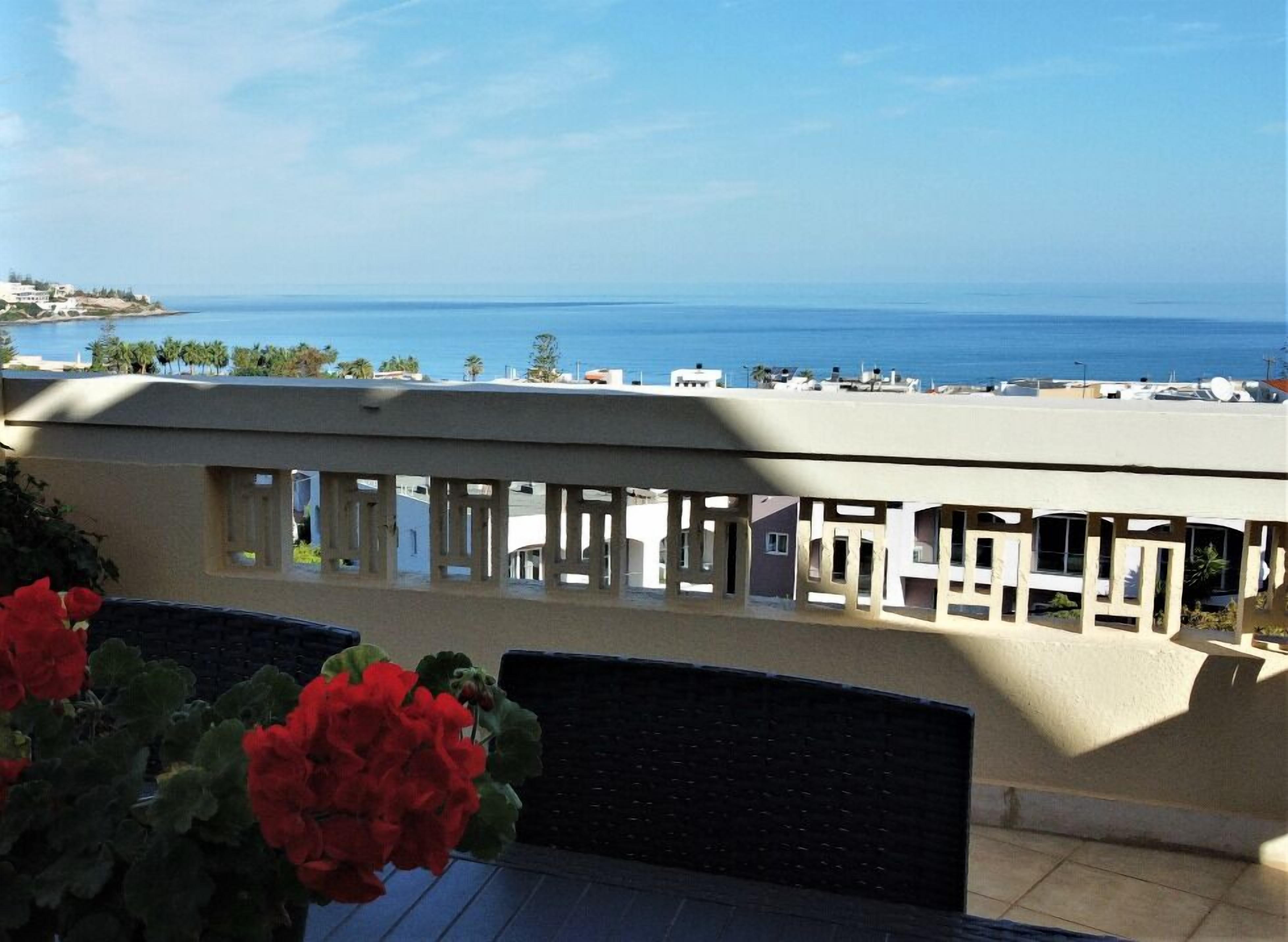 A balcony with a view of the sea and buildings in the distance.